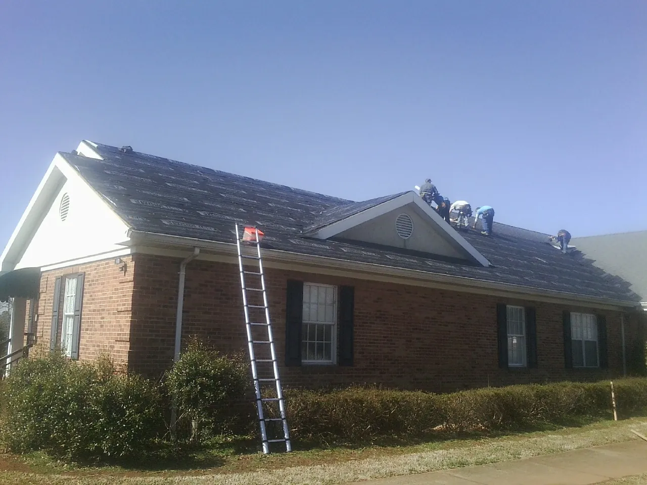 Crew tearing shingles off a brick ranch roof with a ladder set — Emergency Roof Repair work by our crew in Portage Des Sioux