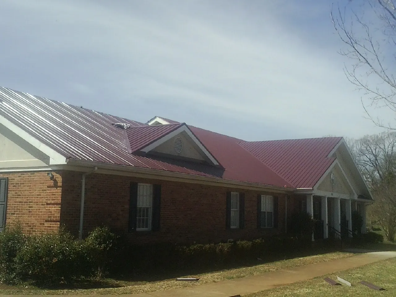 Red metal roof with gabled entries on a long brick building, from a Hail Damage Roof Repair job in Portage Des Sioux