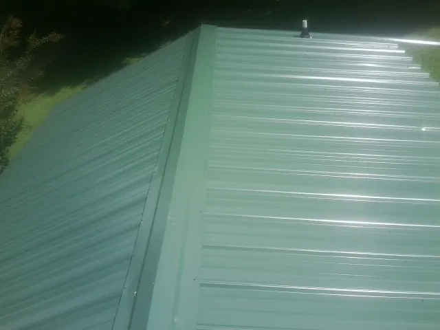 New green metal panels meeting at the ridge of a roof — Flat Roof Repair work by our crew in Portage Des Sioux