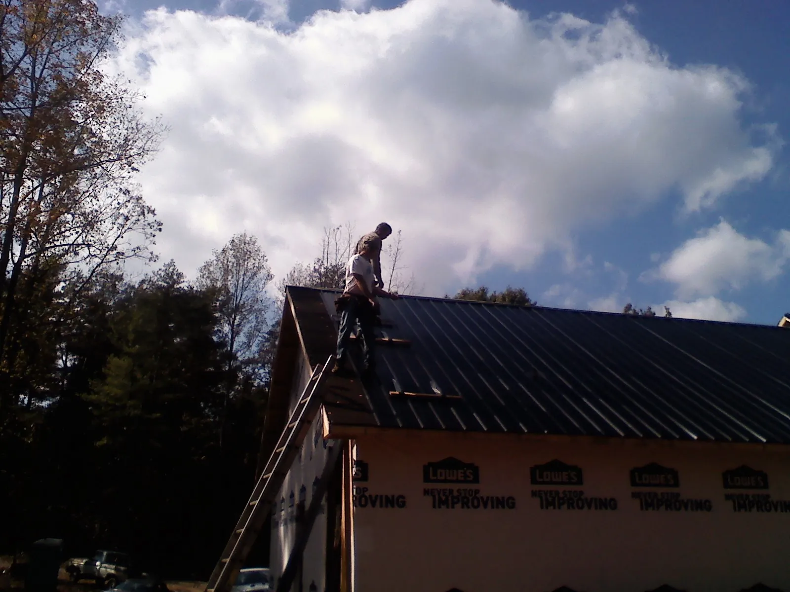 Roofer fastening dark metal panels high against a cloudy sky, from a Roof Inspection job in Portage Des Sioux