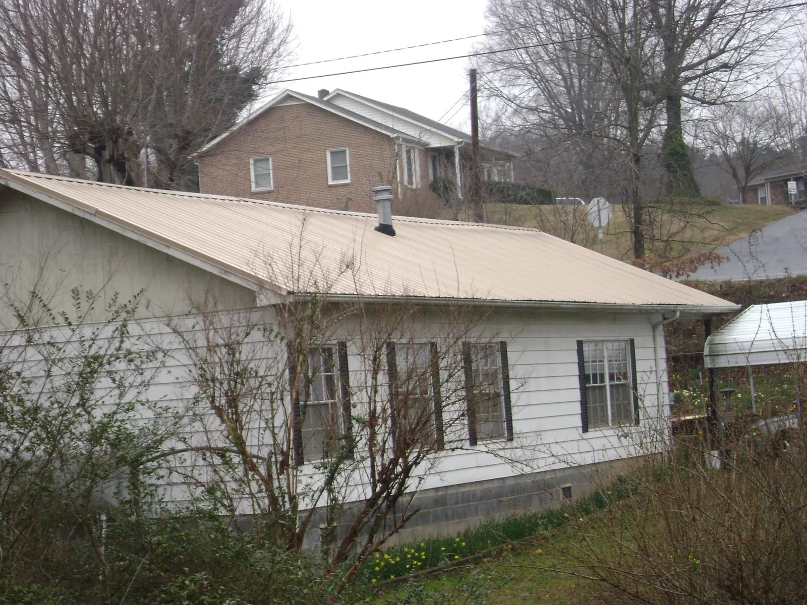Tan metal roof on a white sided house set into a hillside — Commercial Roofing by Roofing Brothers in Portage Des Sioux