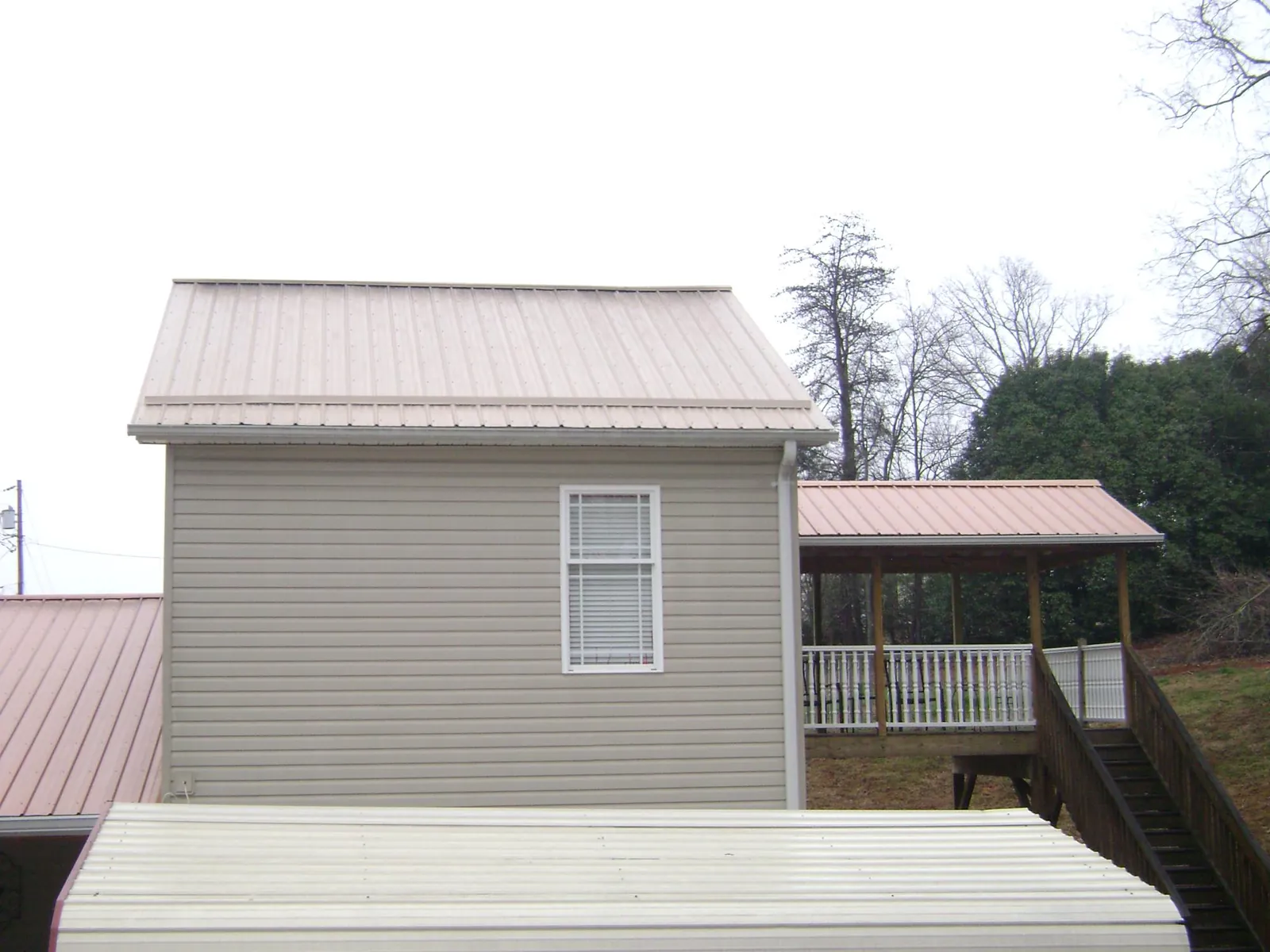 Tan metal roofs on a two story addition and attached porch, from a Roof Replacement job in Portage Des Sioux